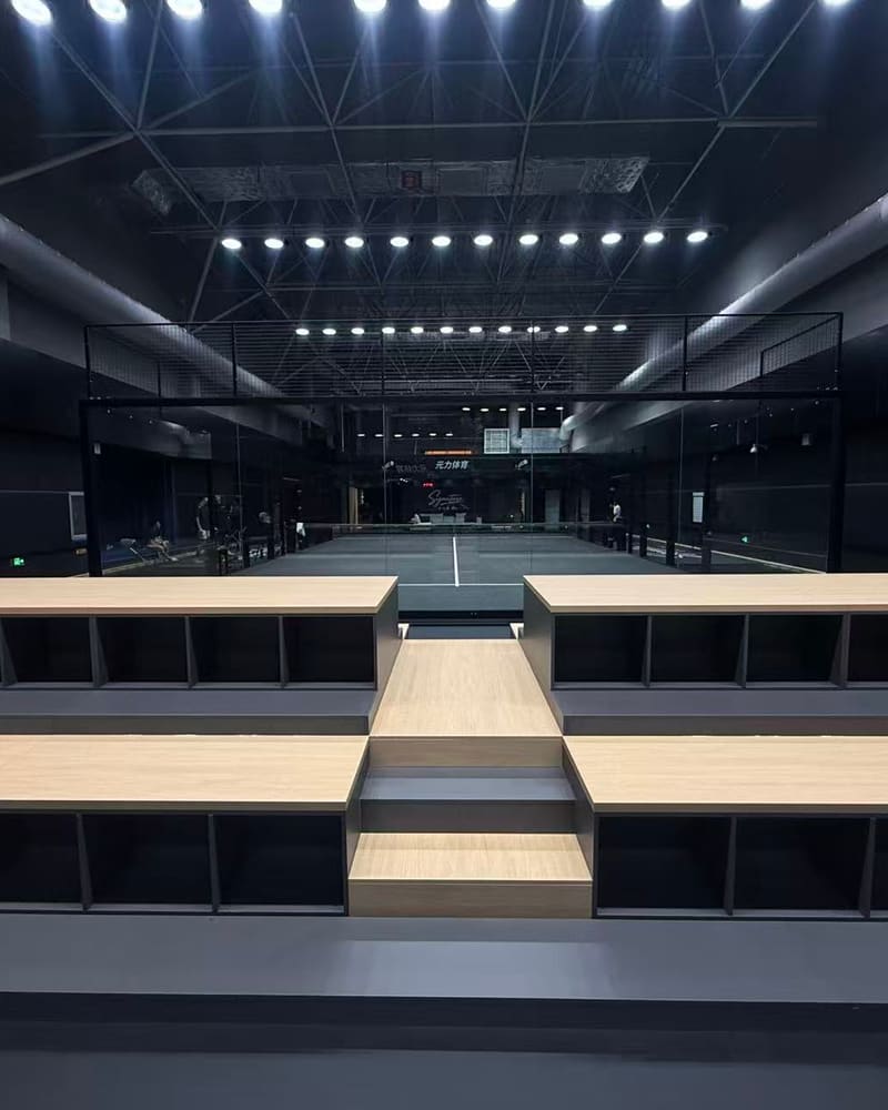 Tiered wooden spectator seating facing a glass court